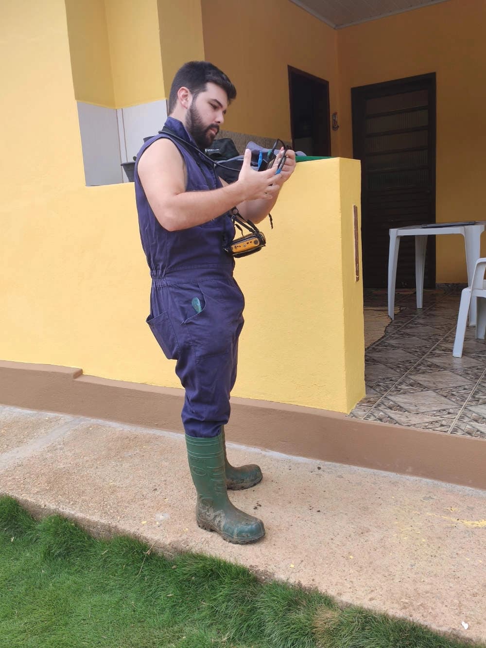 Consultor em macacão e botas de borracha manuseando equipamento de ultrassom em propriedade rural.