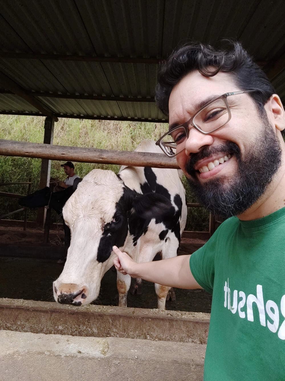 Selfie de integrante da equipe Rehsult sorrindo ao lado de uma vaca, no curral da propriedade.